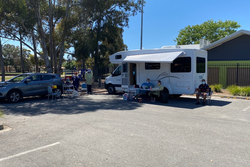 A parked motorhome surrounded by several people wearing PPE and facemasks.