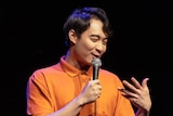 Nigel Ng on stage with a microphone in his hand. 