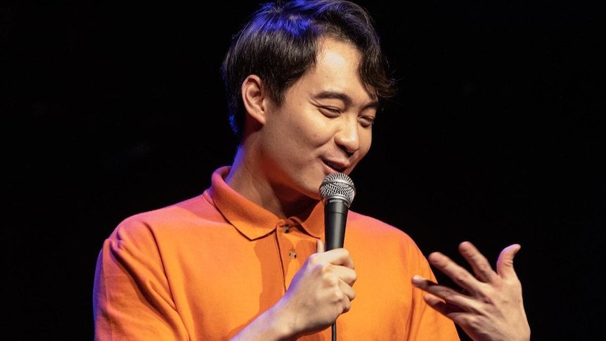 Nigel Ng on stage with a microphone in his hand. 