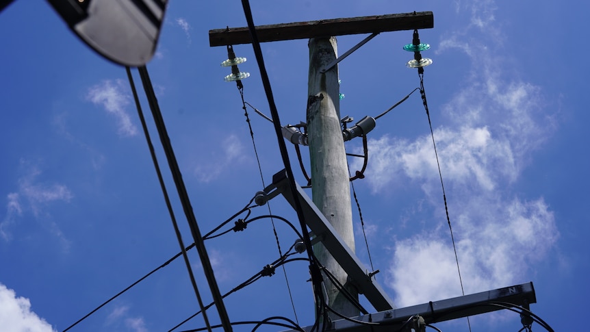 A low shot of a power pole, looking up at the blue sky. 