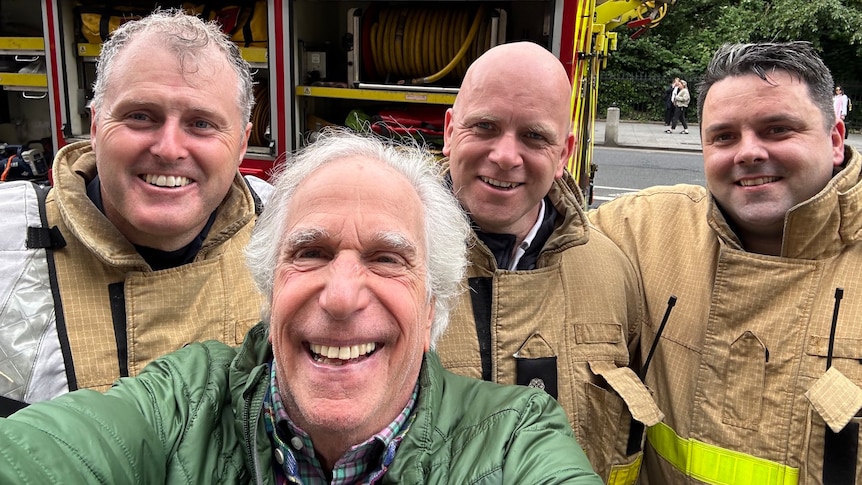 Hollywood actor Henry Winkler in a green jacket with three firefighters in front of a Dublin Fire Brigade truck.