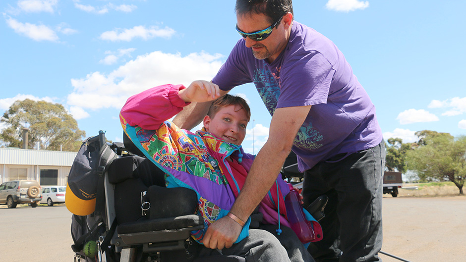 Shanniah Barker puts on a brightly coloured jacket with the help of her father David as she sits in her wheelchair.