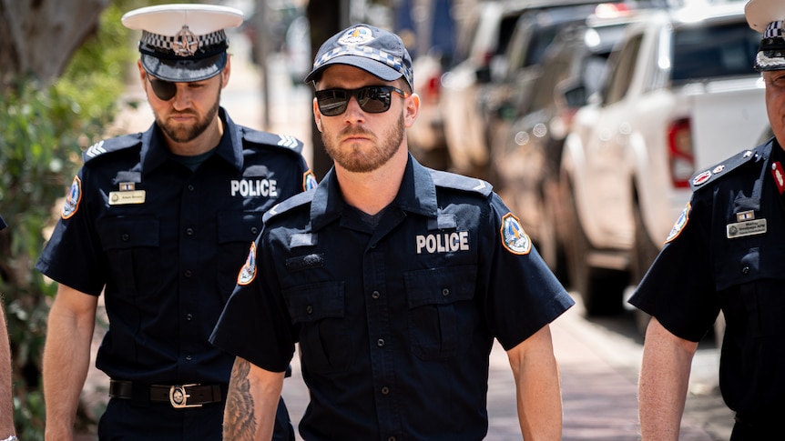 A在阳光明媚的日子里，穿着北领地警察制服的男子走在街上。” class=