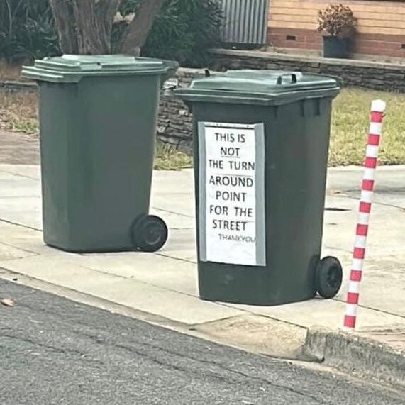 tywo green bins at end of a suburban driveway, one with sign attached to it warding off people making a u-turn