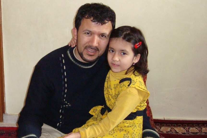 A man and a young girl sit on a carpet and look at the camera