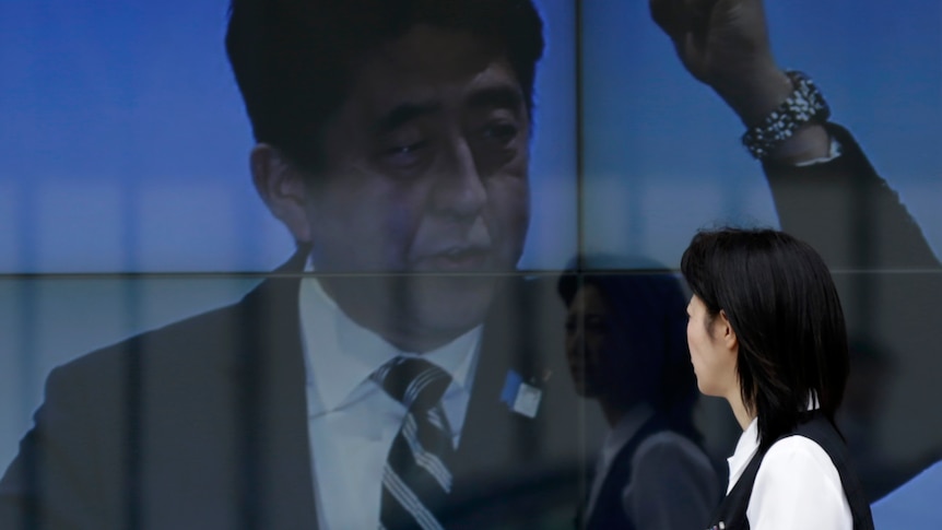 A woman walks past an electronic board displaying a photo of Shinzo Abe
