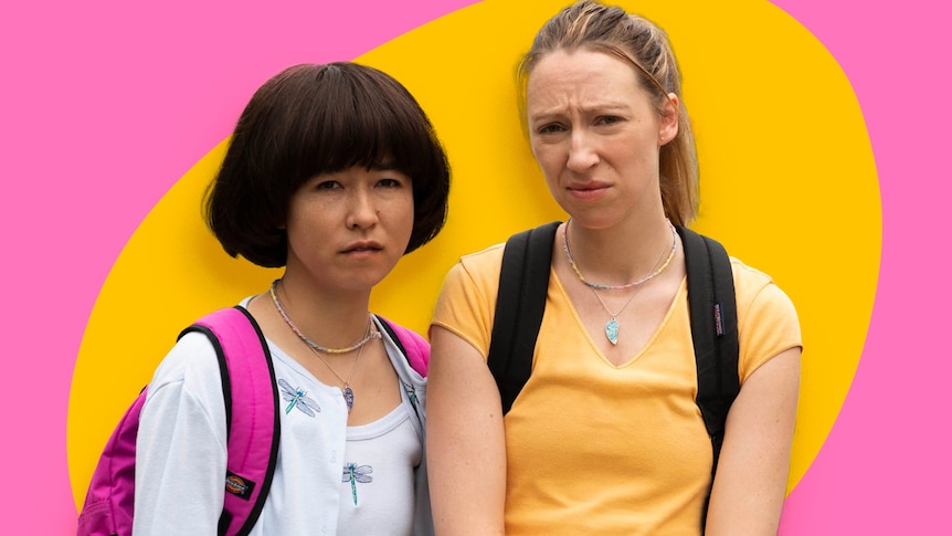 Two women pretending to be teenage girls stand awkwardly wearing t-shirts and backpacks, cut out against a pink, yellow backdrop