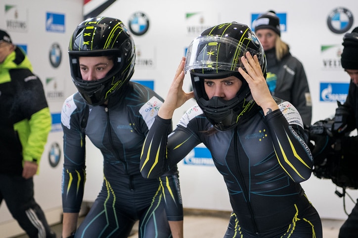 Bree Walker and Stefanie Fernandez look on at the start of a bobsleigh race.