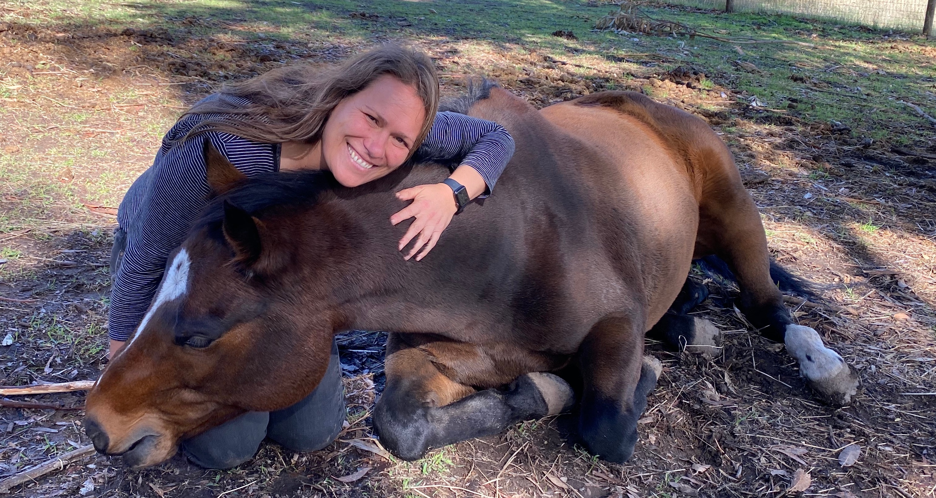 A kneeling woman hugs the neck of a horse.