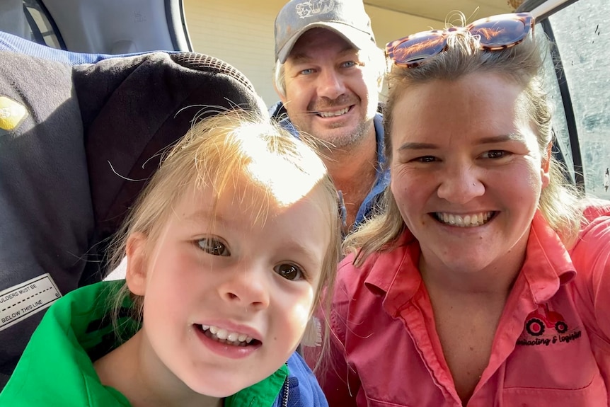 A young girl, her father and mother huddle together in a car and smile