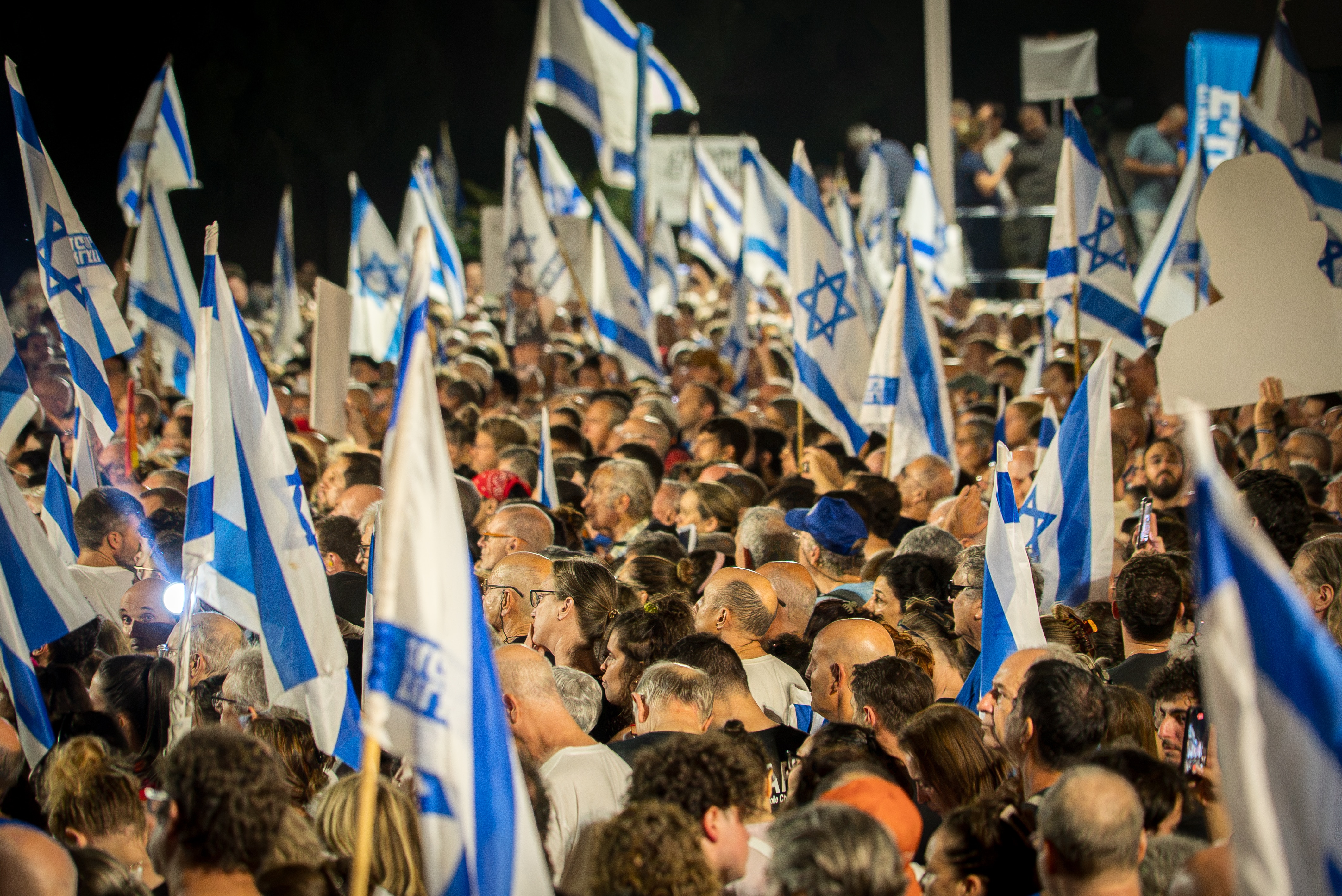 Crowds gather at a rally holding flags and banners.