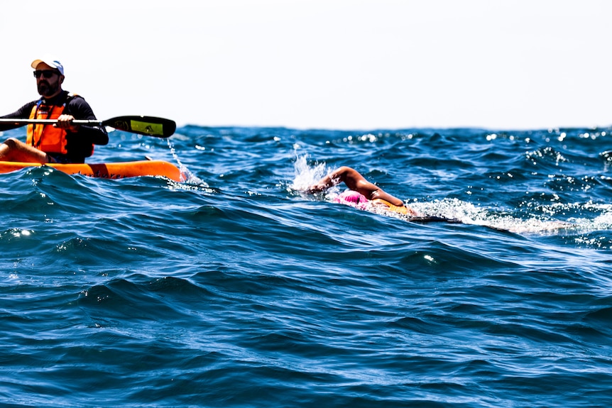 a woman swimming through waves and a kayaker nearby.