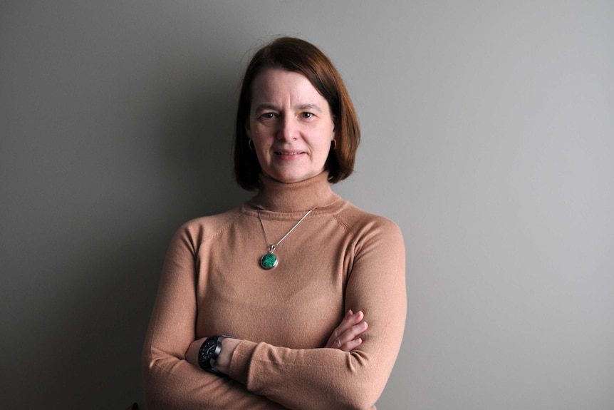 Sylvie Pfieffer stands in front of a grey background with her arms crossed.