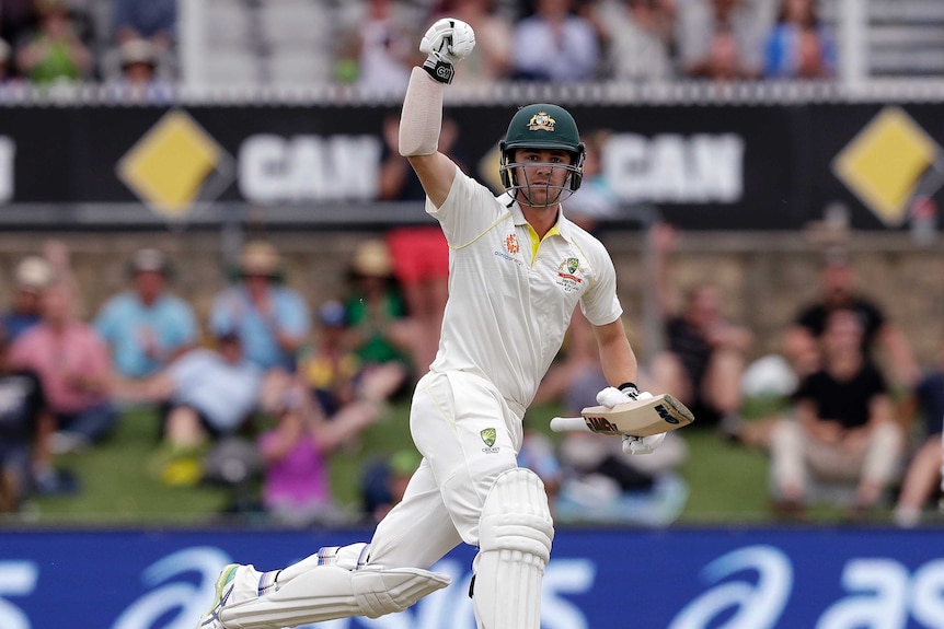 A man runs with his fist clenched in the air above his head, carrying a cricket bat in his other hand.