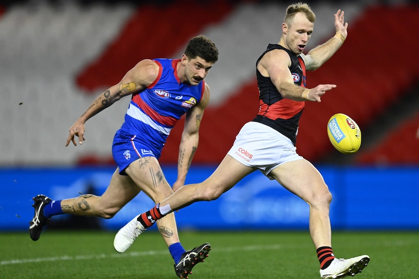 An AFL player kicking the ball with his opponent behind him