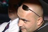 Hizir Ferman sits in a car with his sunglasses on his head. Another man in a tie and white shirt sits next to him.