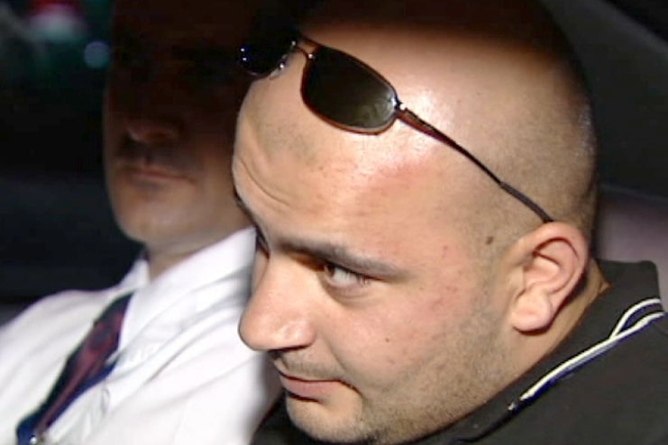 Hizir Ferman sits in a car with his sunglasses on his head. Another man in a tie and white shirt sits next to him.