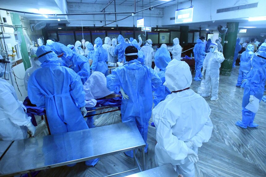 A group of medical personnel wear blue personal protective gear and stand by as injured people arrive.