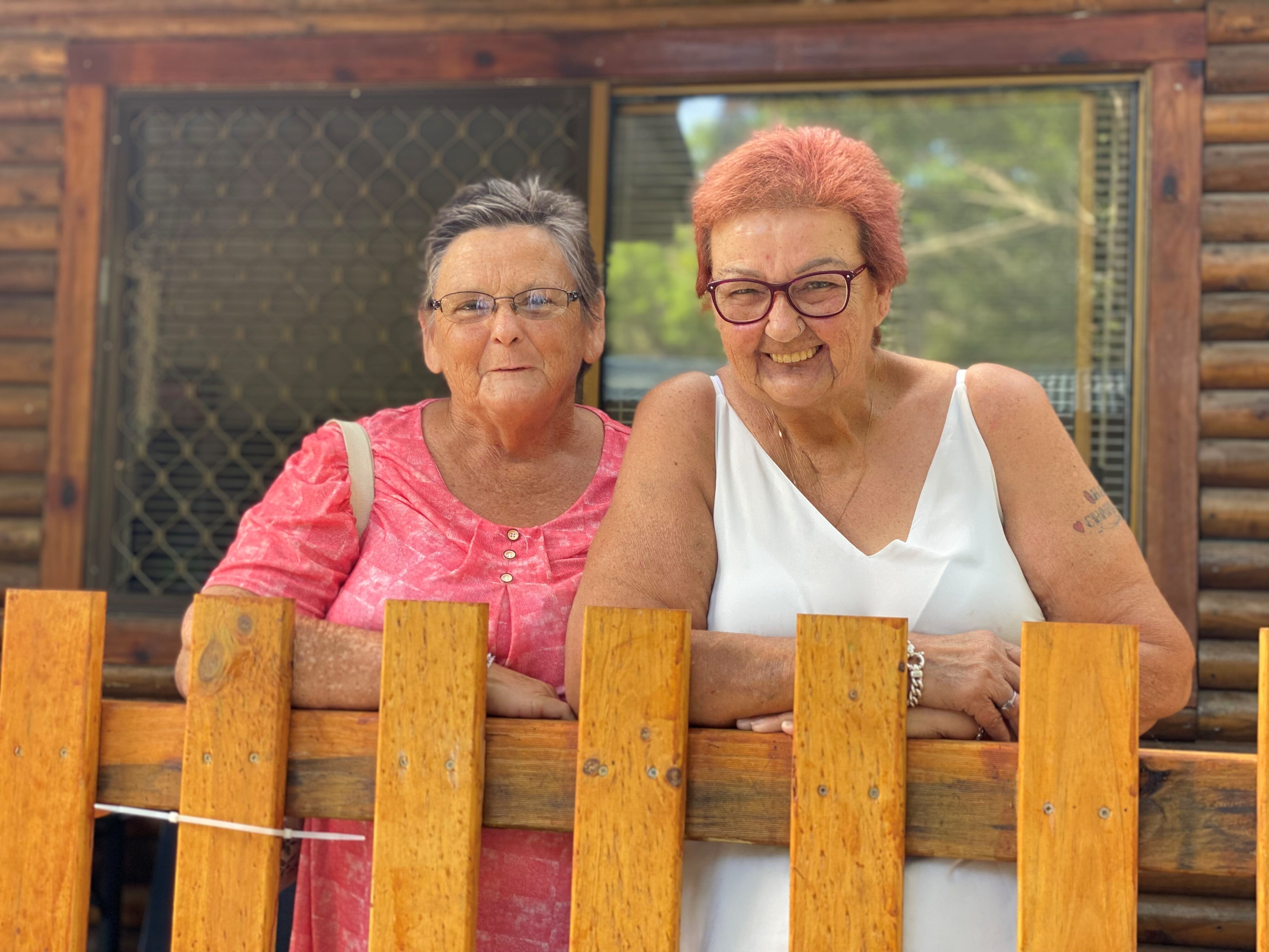 Two women standing on balcony of a cabin. Woman on left is wearing pink top and women on left win white singlet.