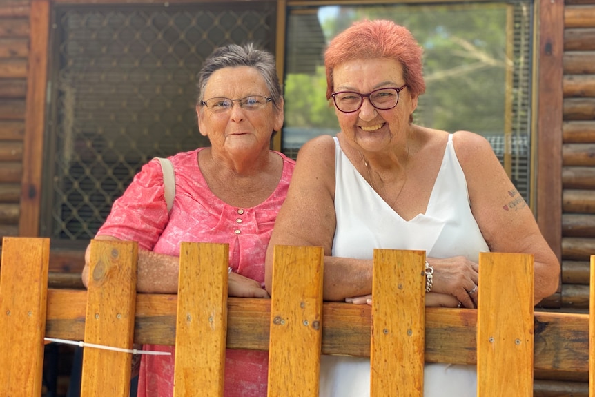 Two women standing on balcony of a cabin. Woman on left is wearing pink top and women on left win white singlet.