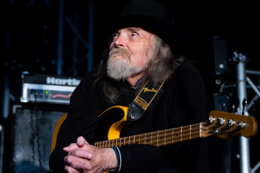 Gavin Webb holds a bass while sitting on stage.