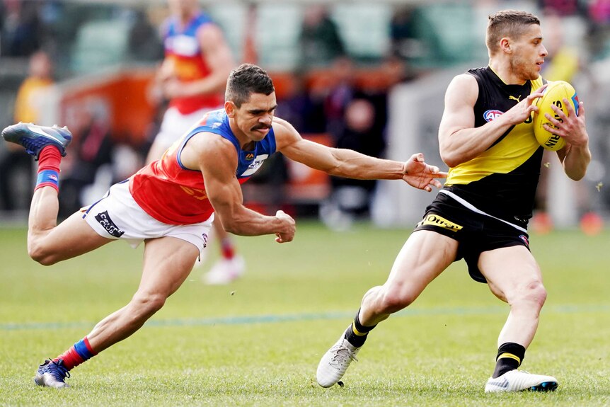 A male AFL player fails to hold on for a tackle on an opposition player, who is holding the ball.