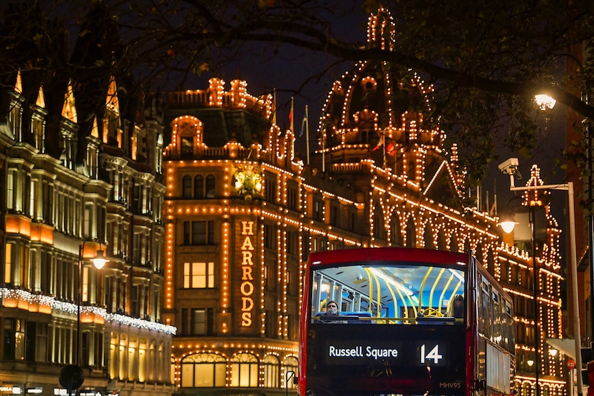 A London red double decker bus drives past the Harrod's store, lit up for Christmas 