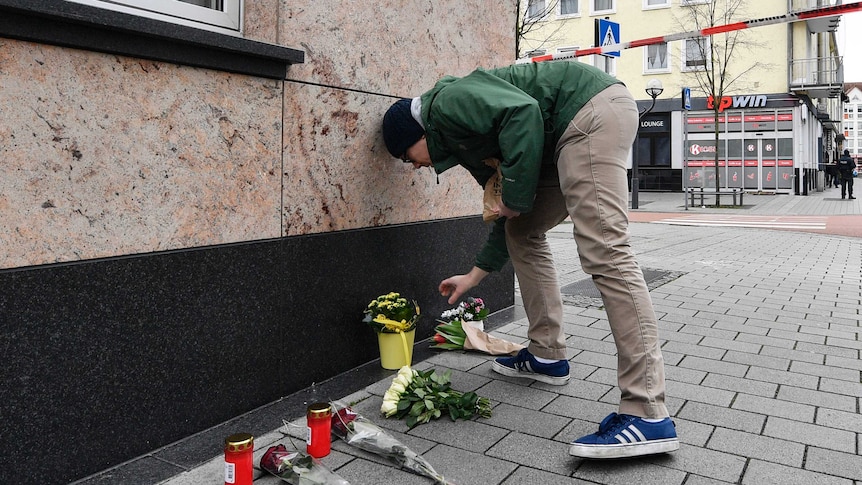 A man places a flower tribute in front of a wall next to other flower tributes
