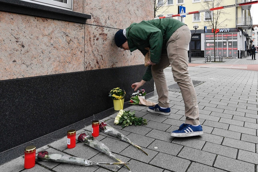 A man places a flower tribute in front of a wall next to other flower tributes