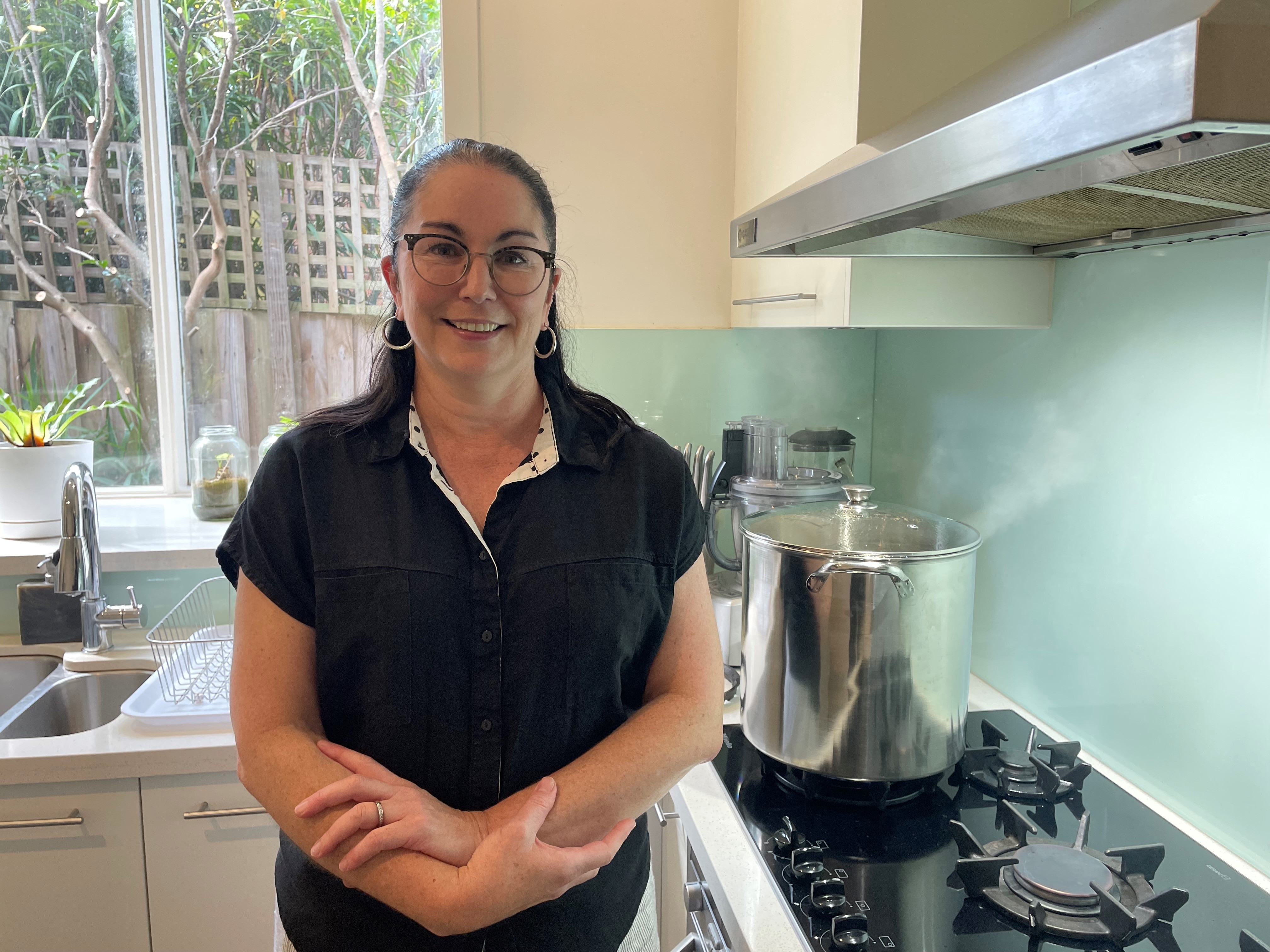 Brigid stands in front of her gas stove while a pot of water is boiling away.
