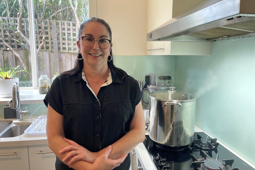 Brigid stands in front of her gas stove while a pot of water is boiling away.