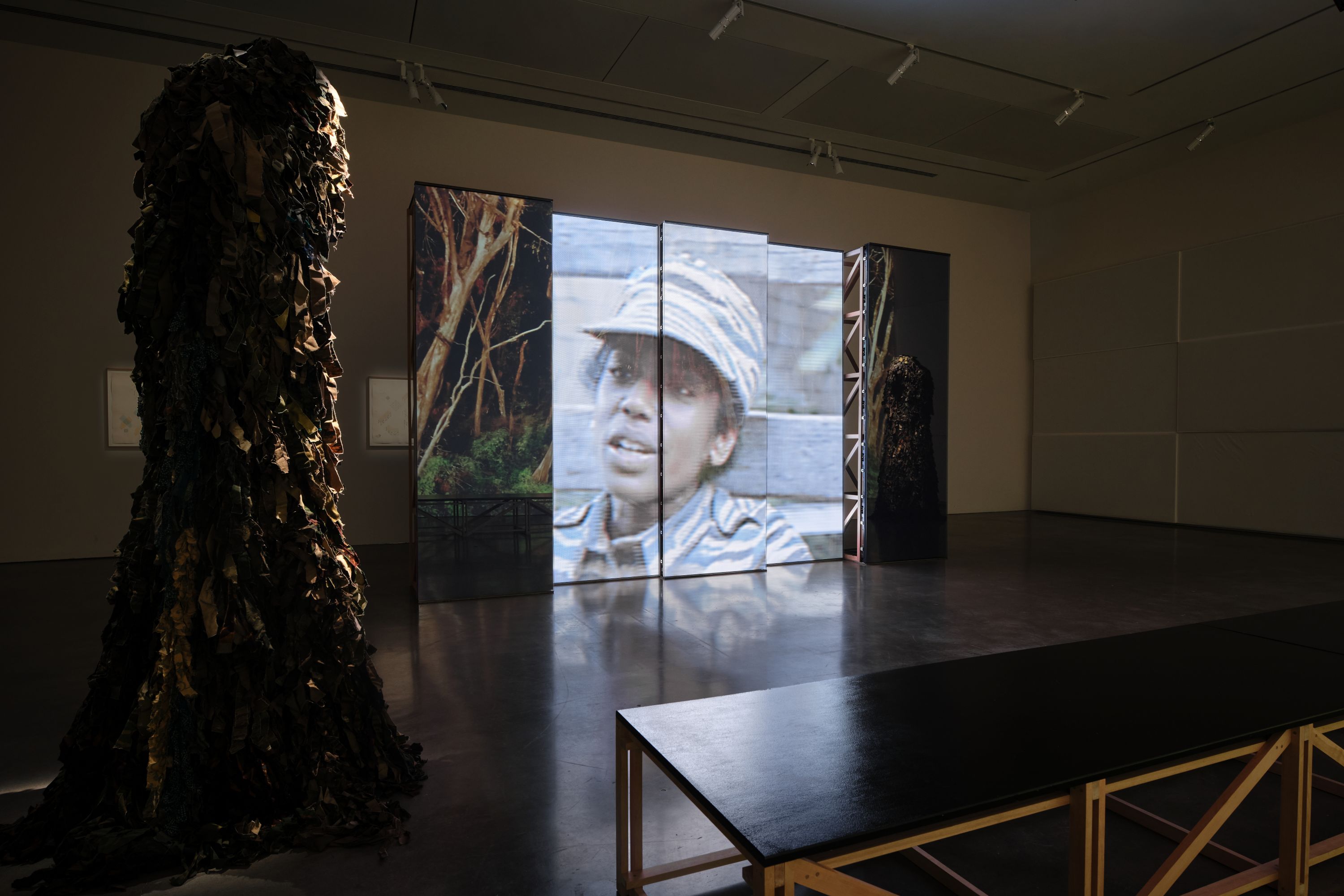 Uma sala com uma tela mostrando uma jovem tâmil vestida com uniforme militar; uma grande escultura está à esquerda