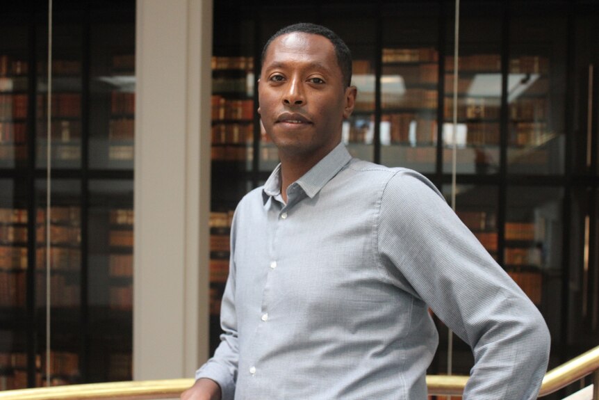 Portrait of a middle-aged man with dark skin wearing a smart buttoned up shirt in a library
