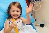 A little girl sits in a hospital bed smiling