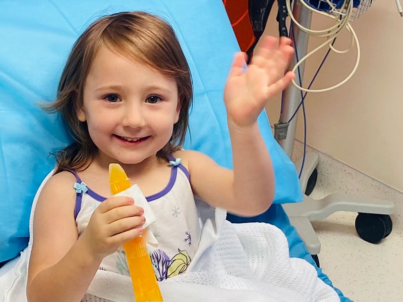 A little girl sits in a hospital bed smiling