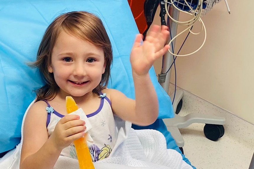 A little girl sits in a hospital bed smiling