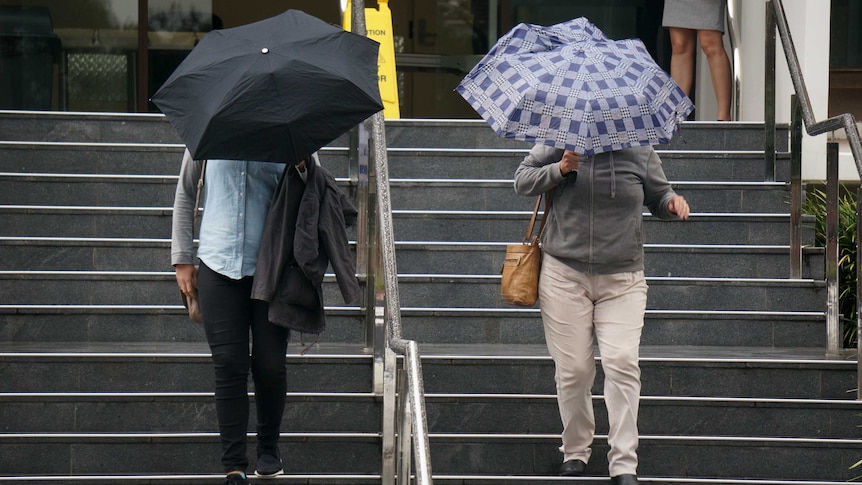 Two women with umbrellas walk down court house stairs.