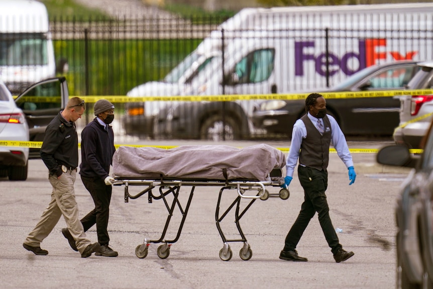 men carry a body on a wheeled stretcher near police tape and a fedex van