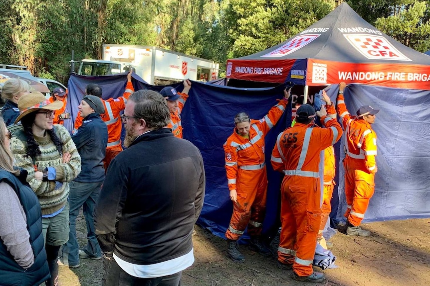 SES volunteers hold up a blue sheet to hide Will and his family from the crowds.