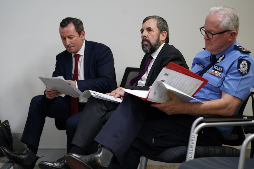 Three government officials sit down and listen to a press conference.