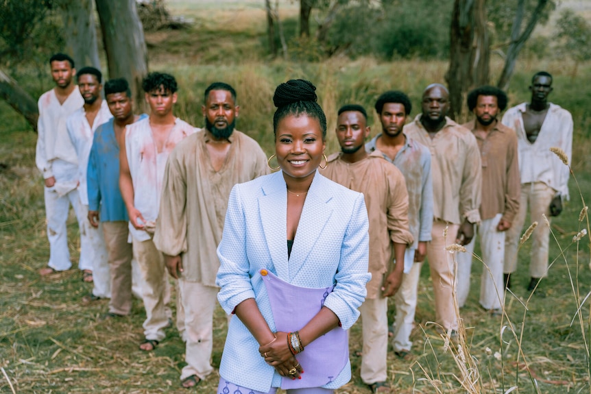 A smiling woman wearing a blue suit with a group of men standing behind her