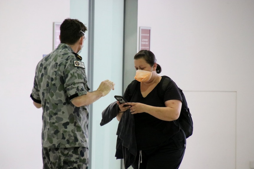 A Border Force official stands with his back facing the camera in front of a woman wearing a mask.