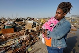 Woman cradles baby while surveying the aftermath of a tornado that destroyed her home.