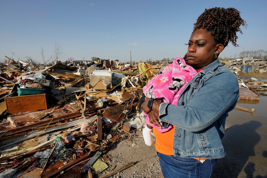 Woman cradles baby while surveying the aftermath of a tornado that destroyed her home.