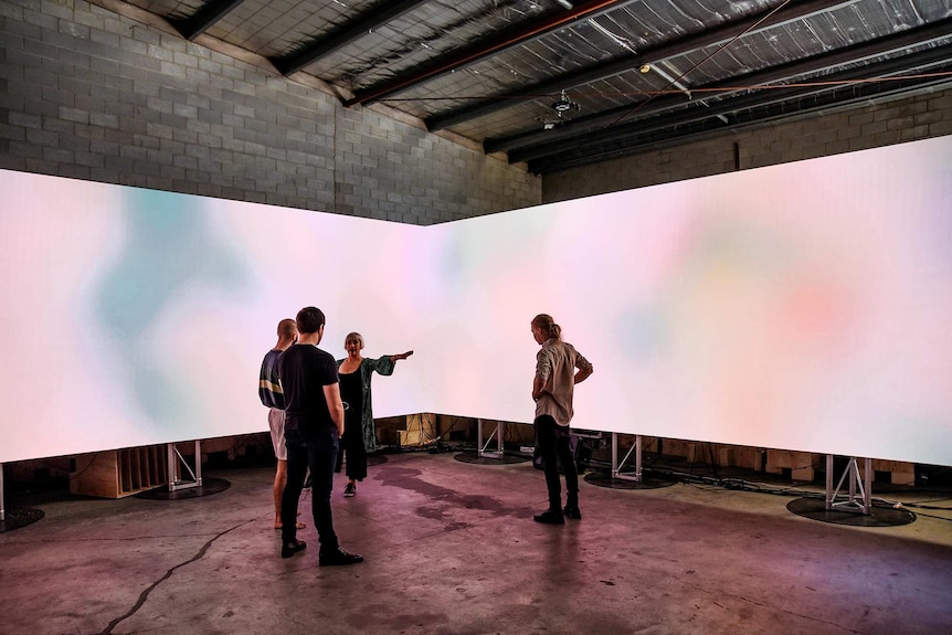 A group of people stand in front of a wide wall of LED light that follows the contours of a rectangular room