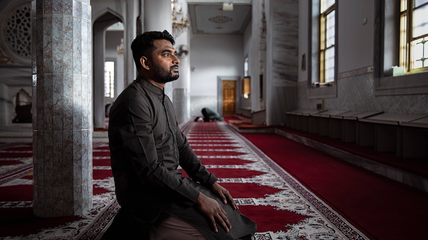 Khaled Shaikh kneels on red carpet inside a mosque during daytime.