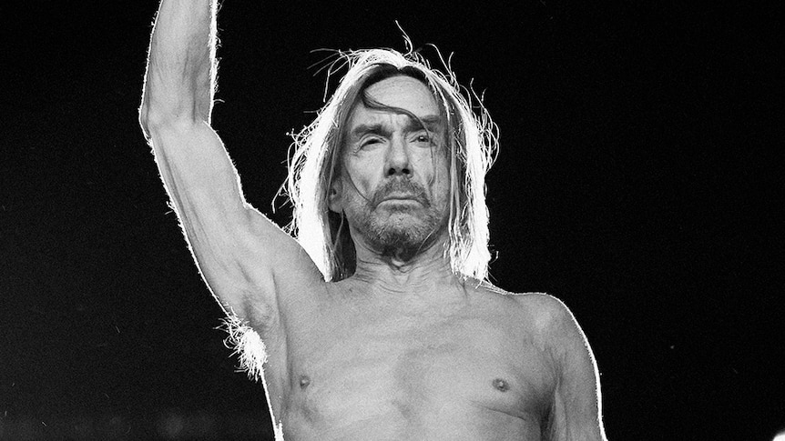 Black and white photo of a shirtless Iggy Pop raising his fist in the air