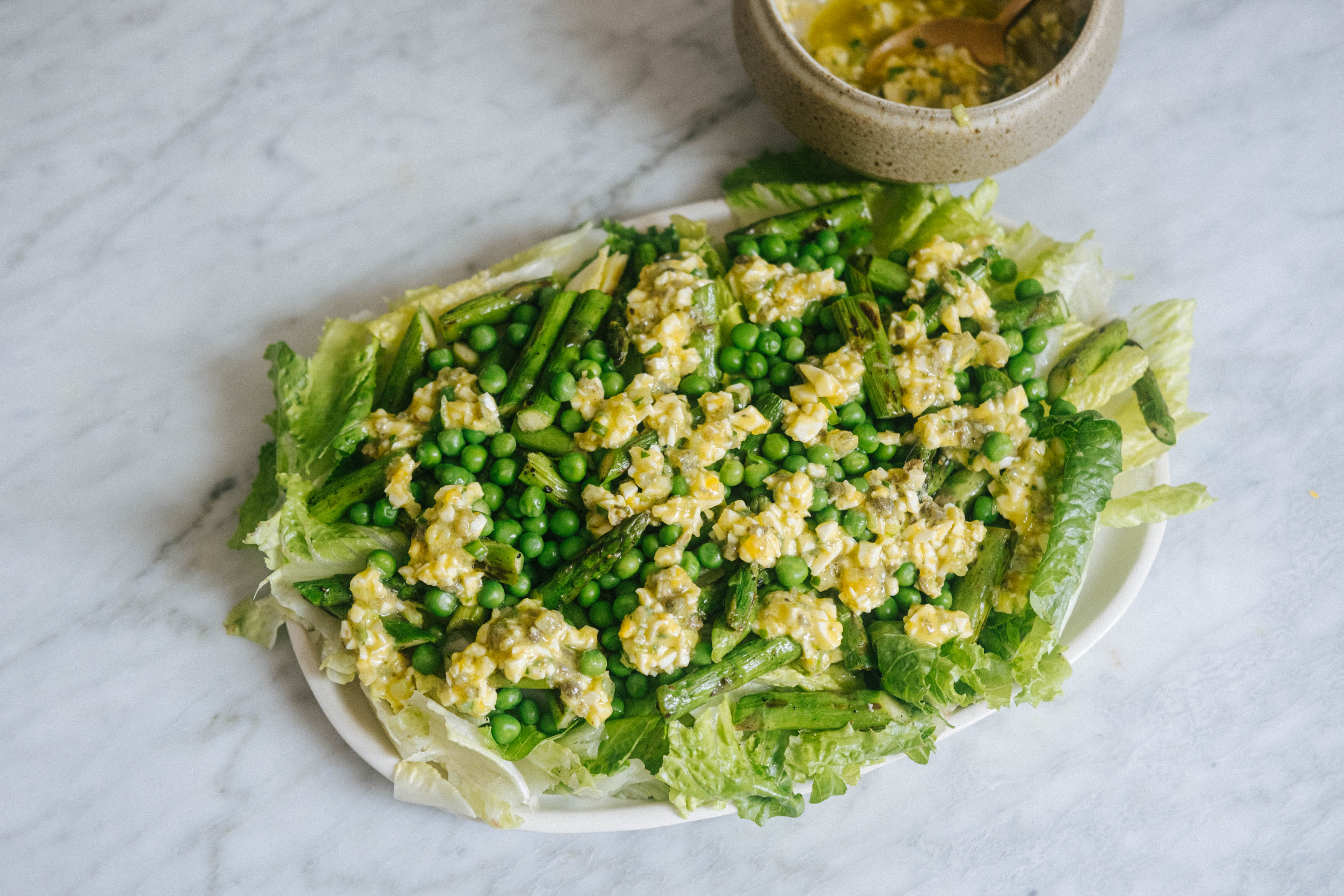 An oblong platter with crunchy chopped lettuce salad with baby peas and sauce gribiche. In a small bowl is more sauce gribiche.