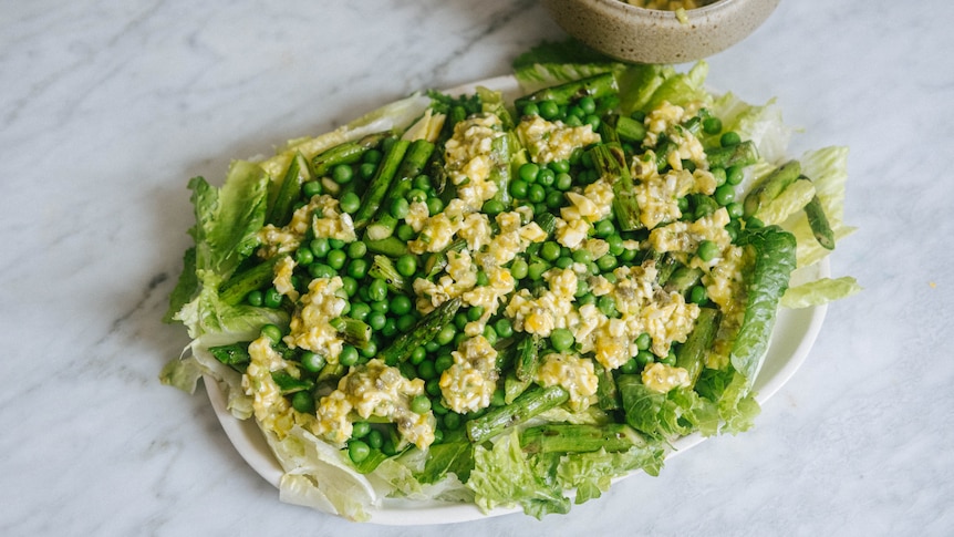 An oblong platter with crunchy chopped lettuce salad with baby peas and sauce gribiche. In a small bowl is more sauce gribiche.