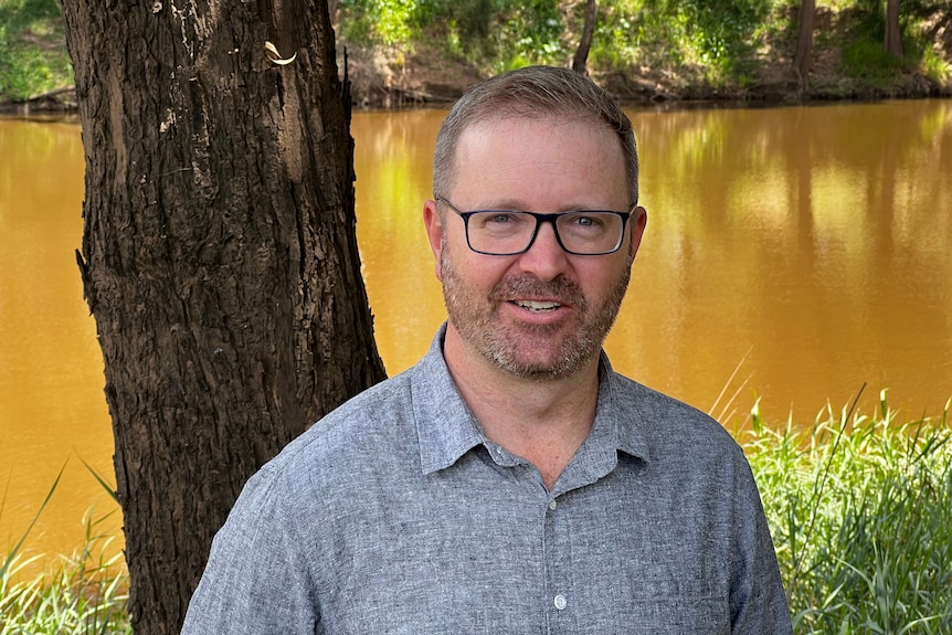 A man standing near tall reeds and a full flowing river